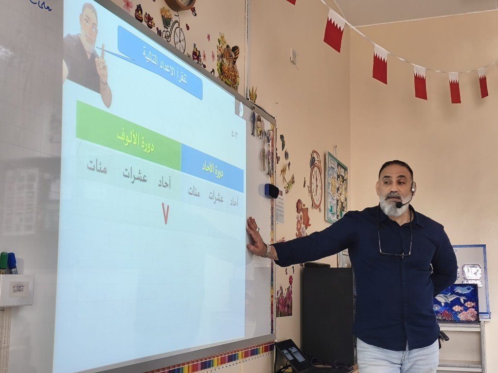 أ. منير علي أثناء شرح الرياضيات على السبورة التفاعلية — درس الأعداد والدورات
